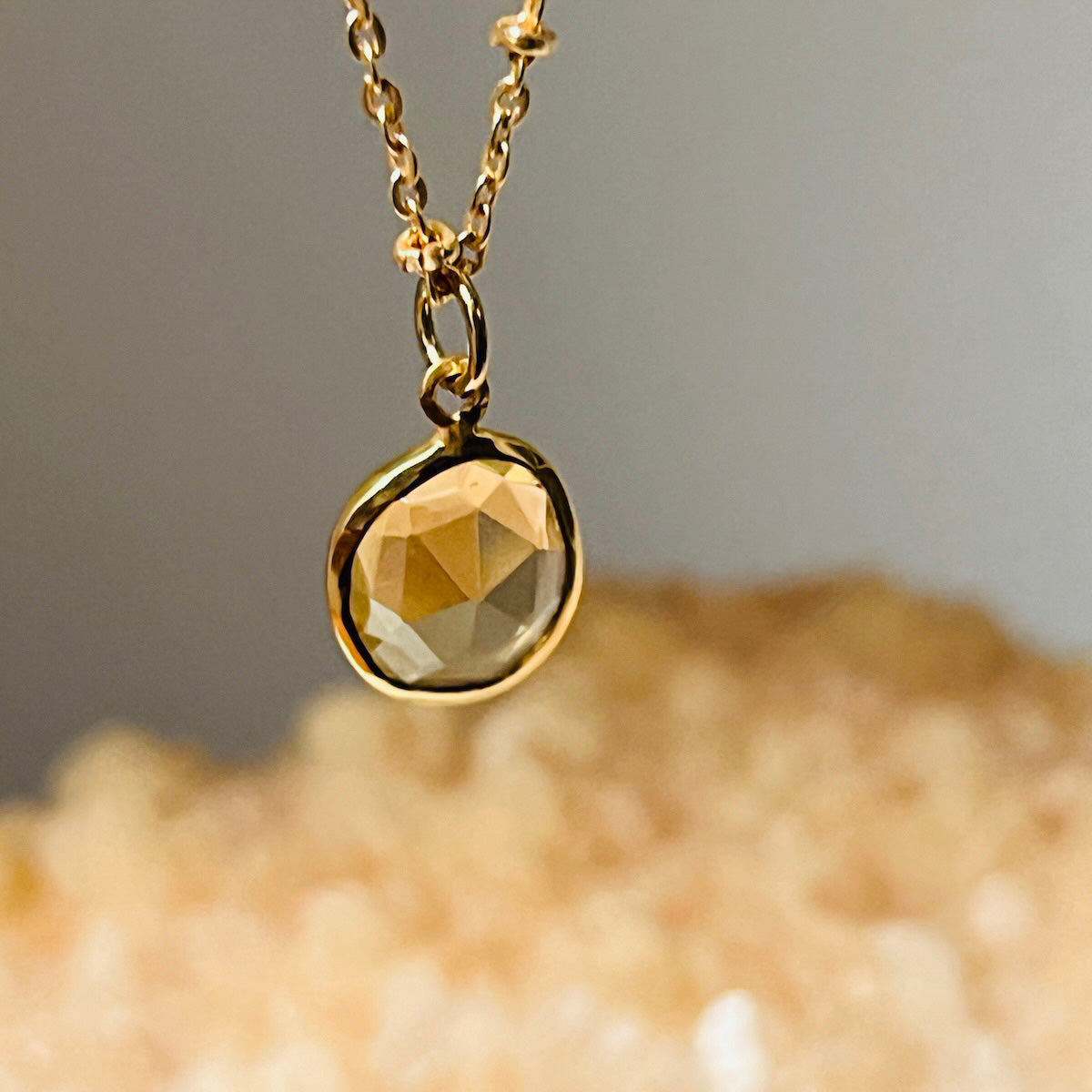 Close up of a gold necklace with a freeform citrine pendant on a neutral background