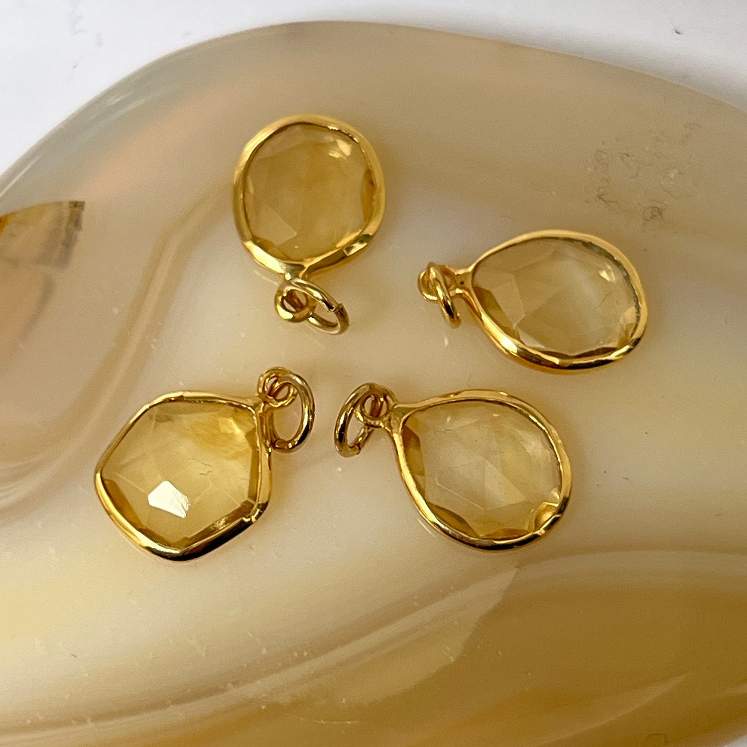 Four gold freeform citriine pendants on a beige dish