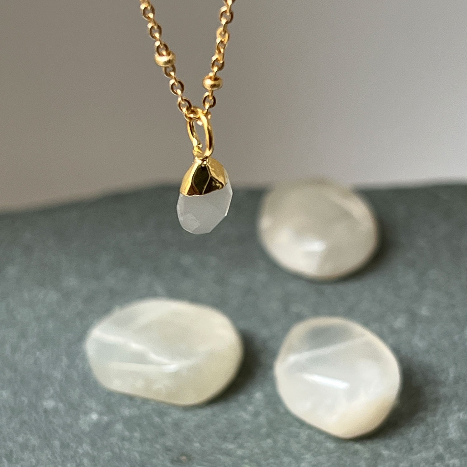A close up of a white moonstone pendant on a gold biba chain, with white crystals in the background