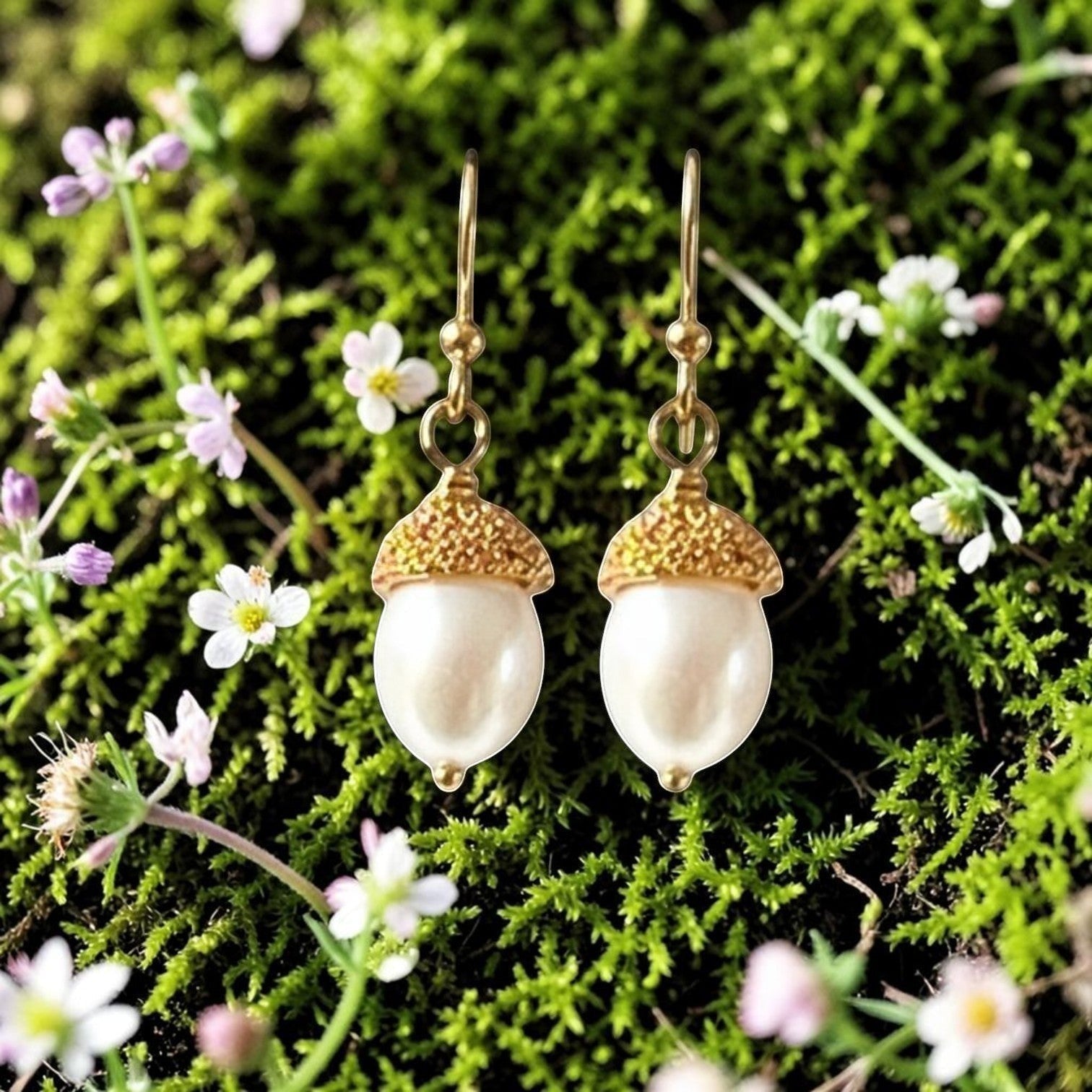 Mirabelle Jewellery white freshwater pearl acorn earrings with granulated gold caps, set against moss and small flowers.