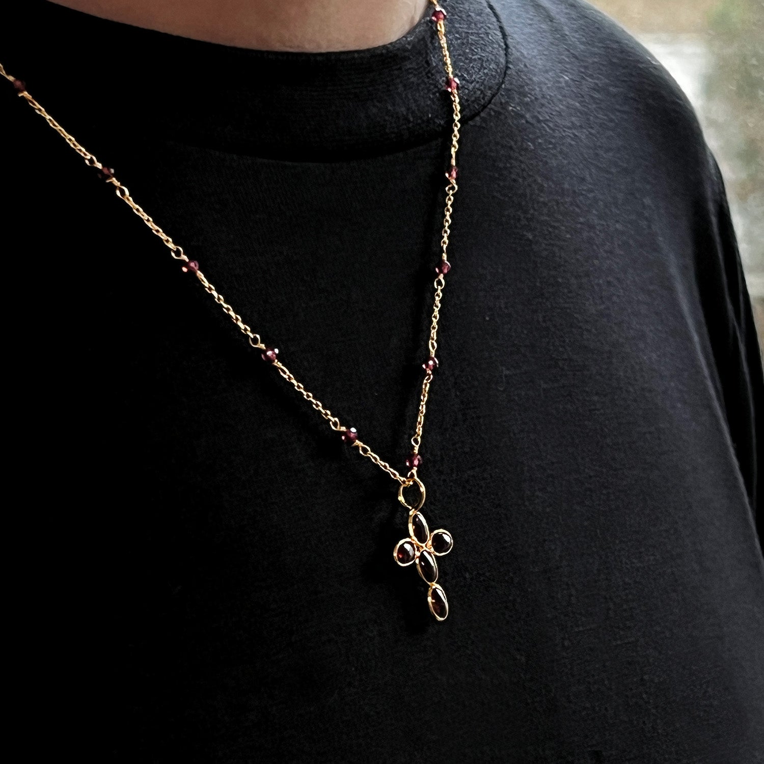Gold necklace with a cross pendant featuring red garnet gemstones on a model wearing a black sweater