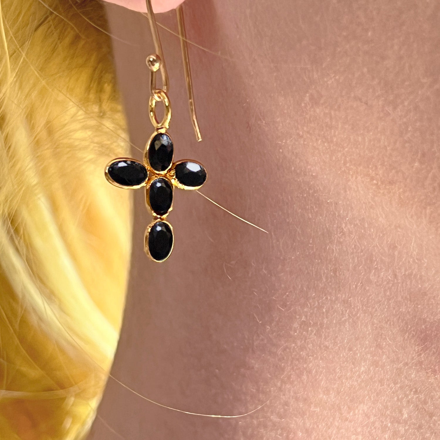 Gold earring with black onyx stones worn by a person with blonde hair.