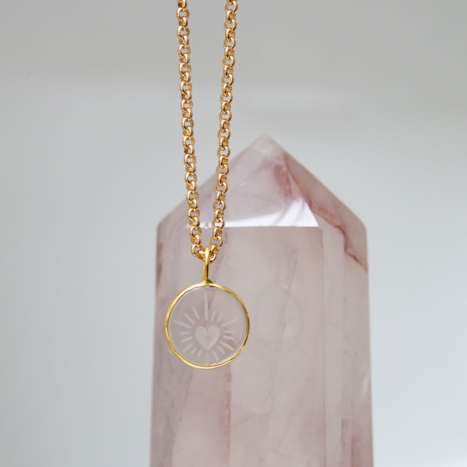 Gold necklace with a heart carved rock crystal pendant on a pink crystal