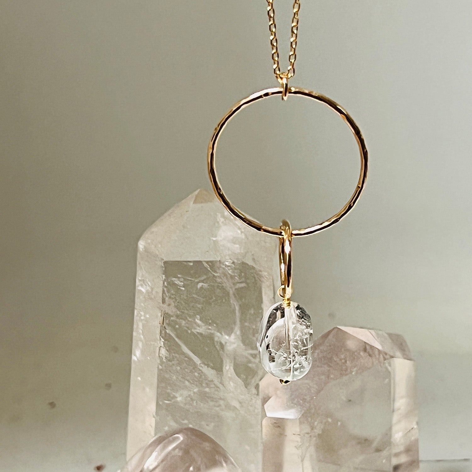 Gold necklace with a freeform rock crystal pendant on a neutral background with a larger rock crsytal