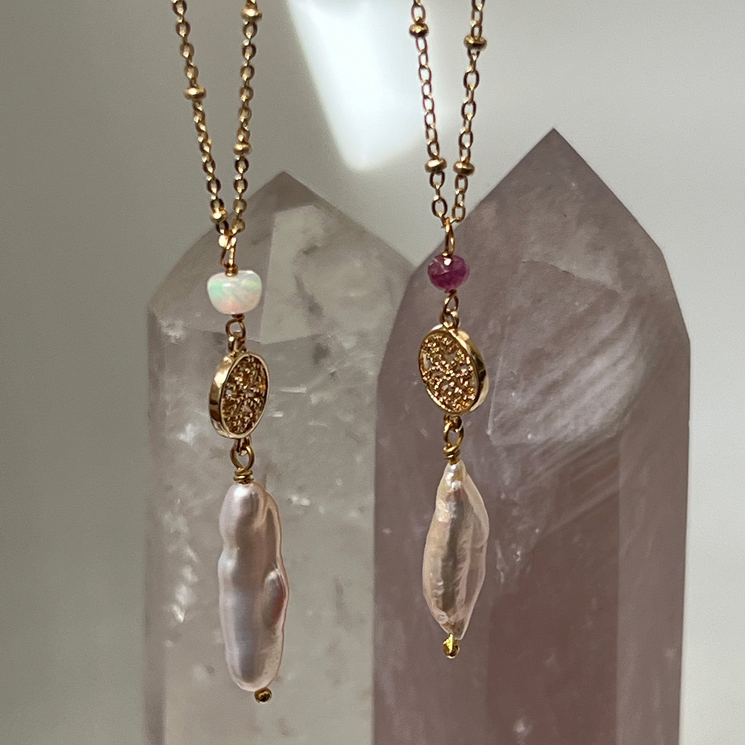 Two gold-plated pendants featuring baroque pearls and opals againsta a crystal background