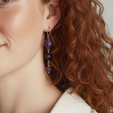 Close-up of a person wearing a gold earring with three purple amethysts.