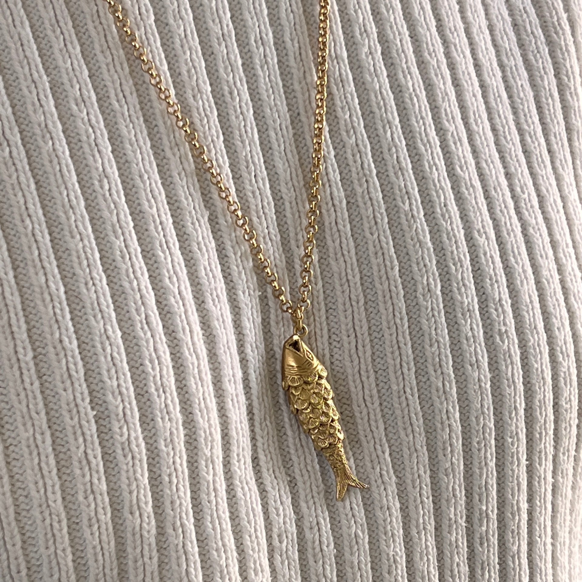 A gold-plated articulated fish charm on a gold satellite chain worn on an ivory jumper