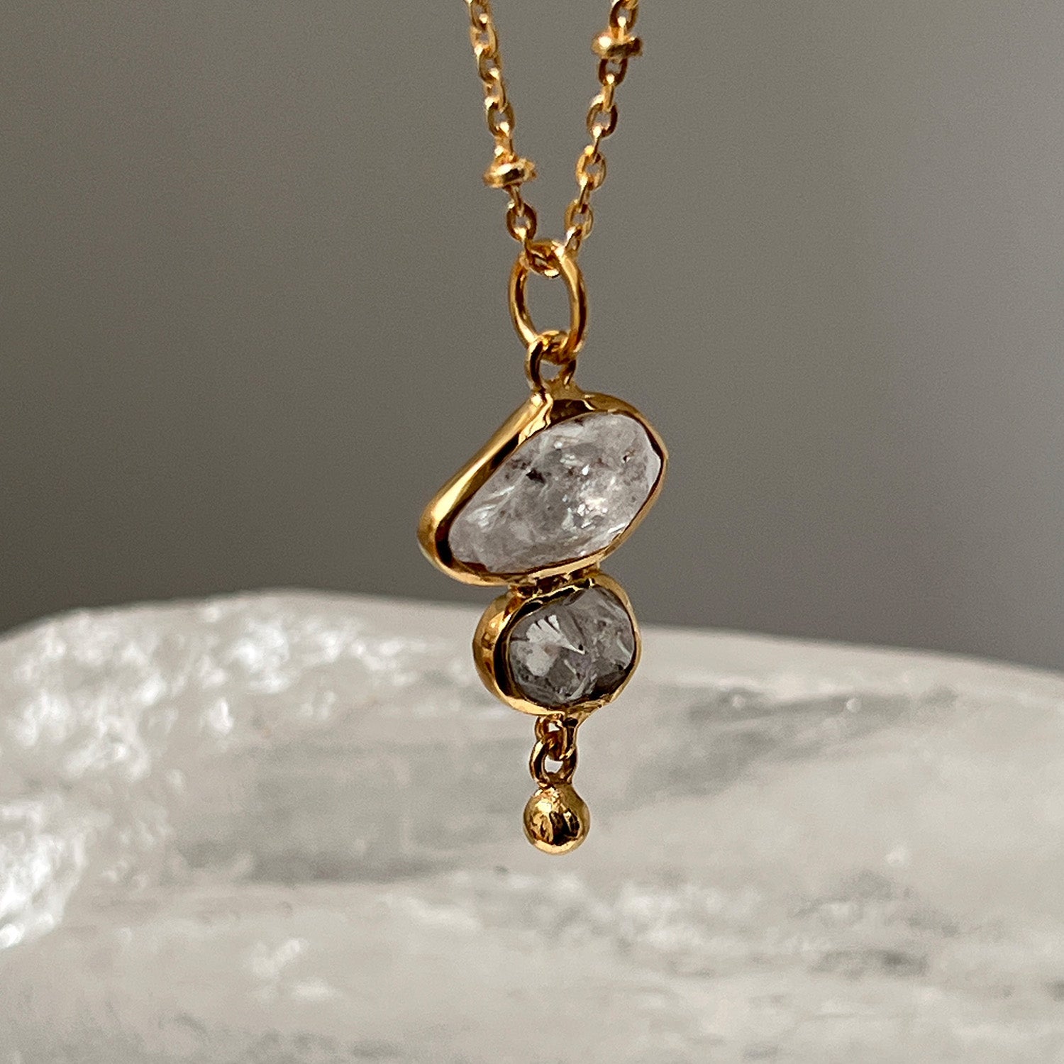 Gold necklace with a pendant featuring clear stones on a textured surface.