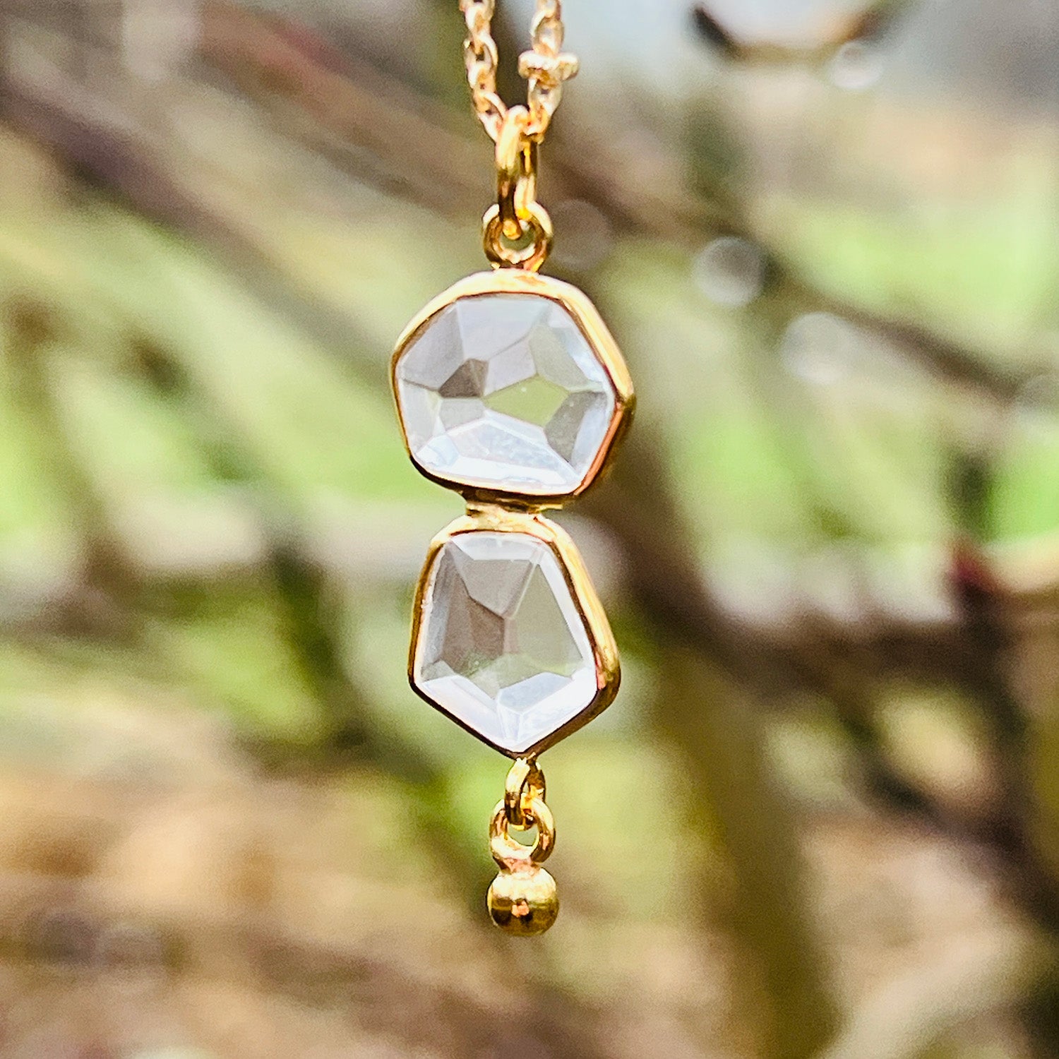 Gold necklace with two clear gemstones against a blurred natural background