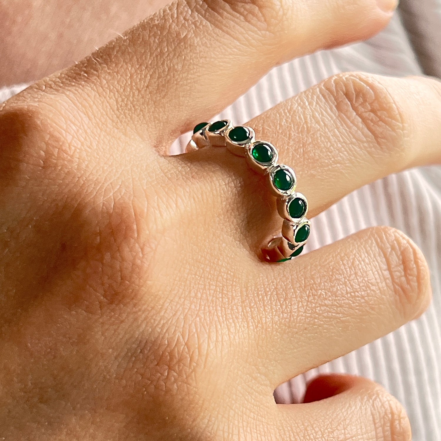 Close-up of a hand wearing a silver ring with green onyx gemstones on a neutral background