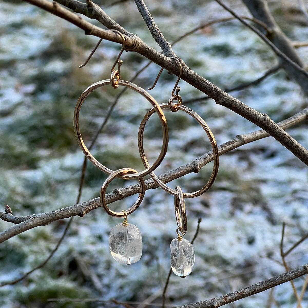 Gold hoop earrings with freeform rock crystals hanging on a branch with snow in the background