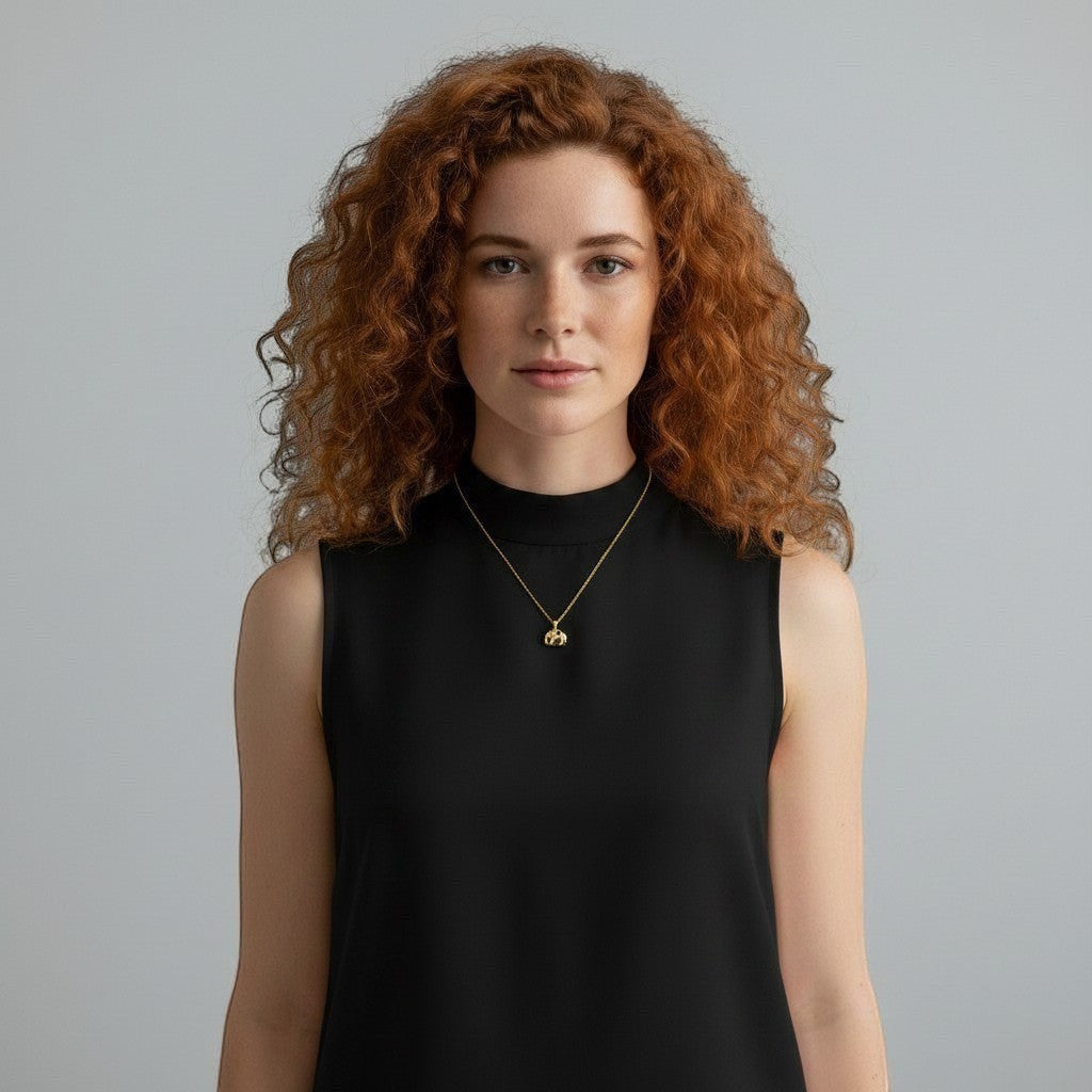 Mirabelle Jewellery tiny 3D elephant pendant with a ruby accent on a long gold-plated chain worn by a red-haired model.