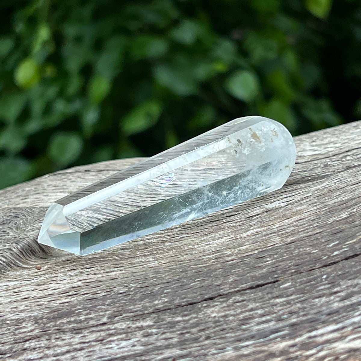 Mirabelle Jewellery clear rock crystal healing wand from Madagascar resting on a rustic wooden surface.