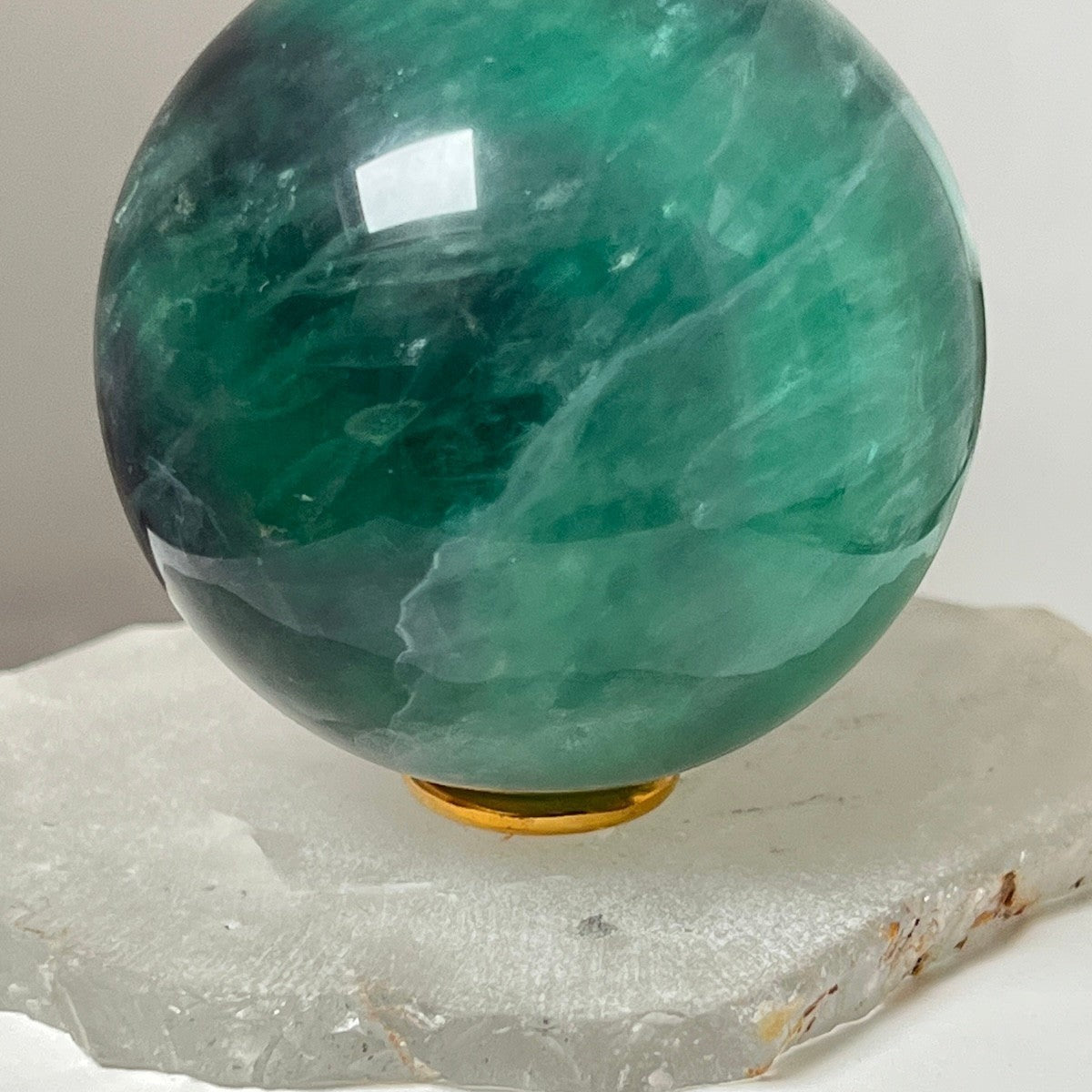 Mirabelle Jewellery polished green fluorite sphere with natural emerald and jade color variations, displayed on a white stone base.