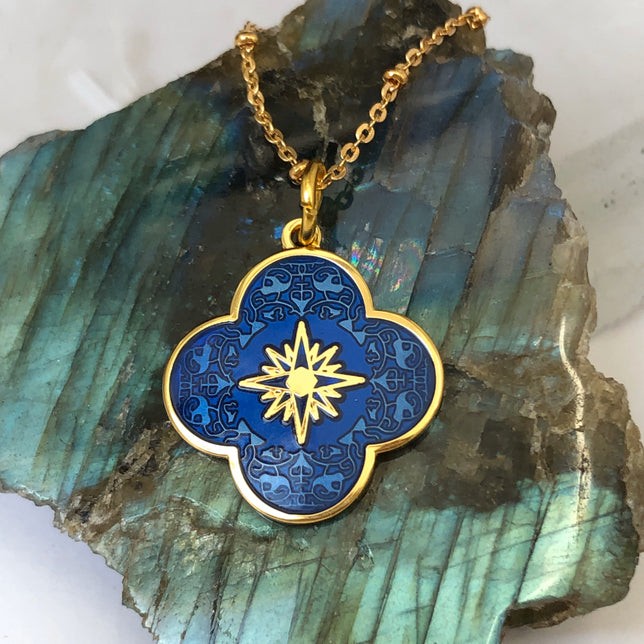 Close up of a royal blue enamel medal with a gold-plated brass cross symbol on the front, featuring a star design at the center, on a crystal