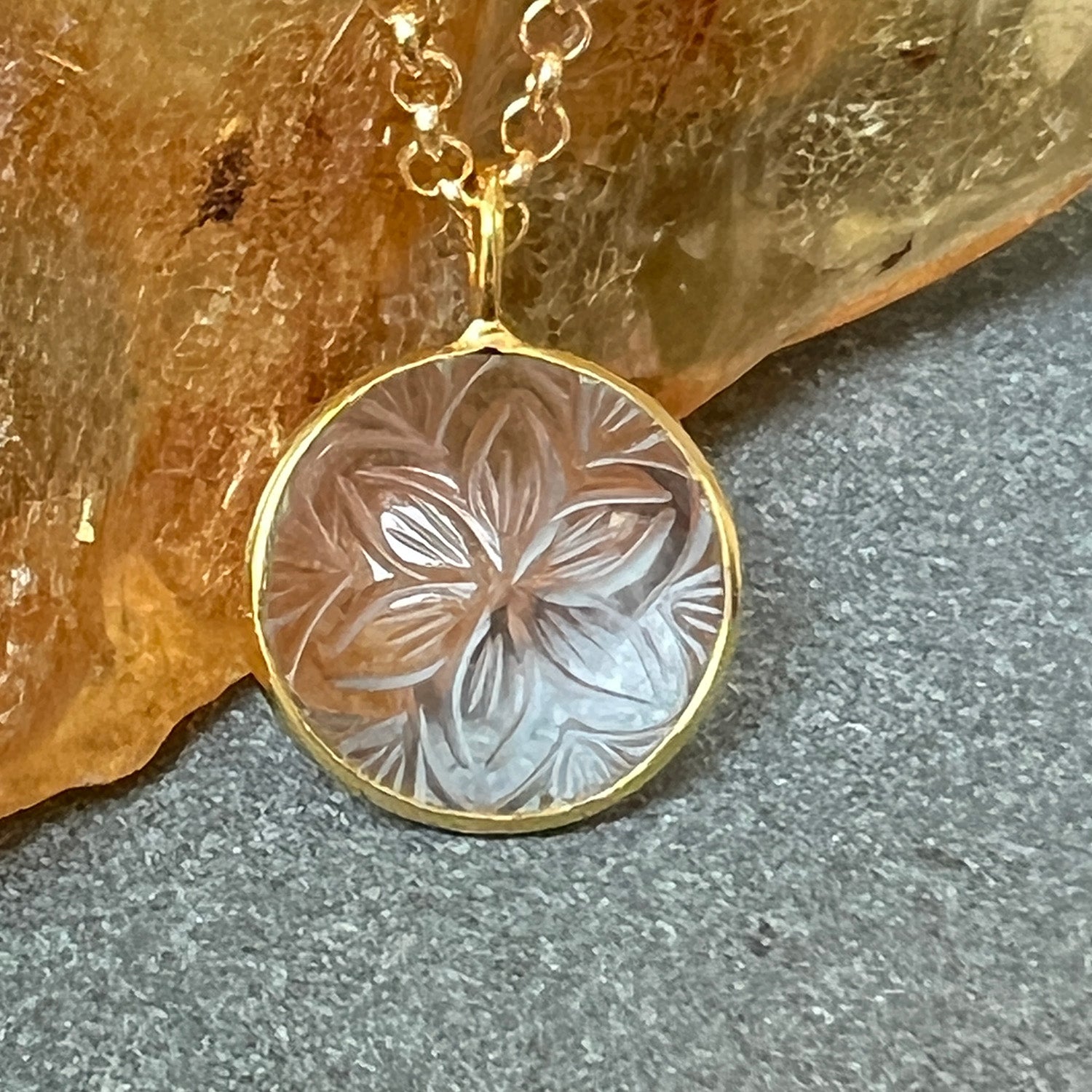 Gold necklace with a round pendant featuring floral engraving on a textured surface.