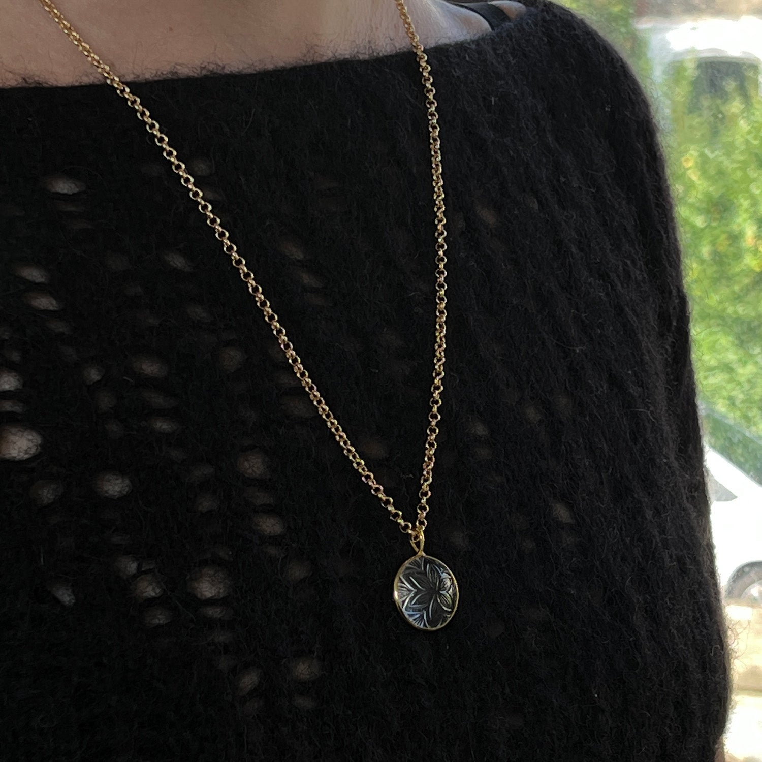 Gold necklace with a hand-carved flowerpendant on a black textured sweater