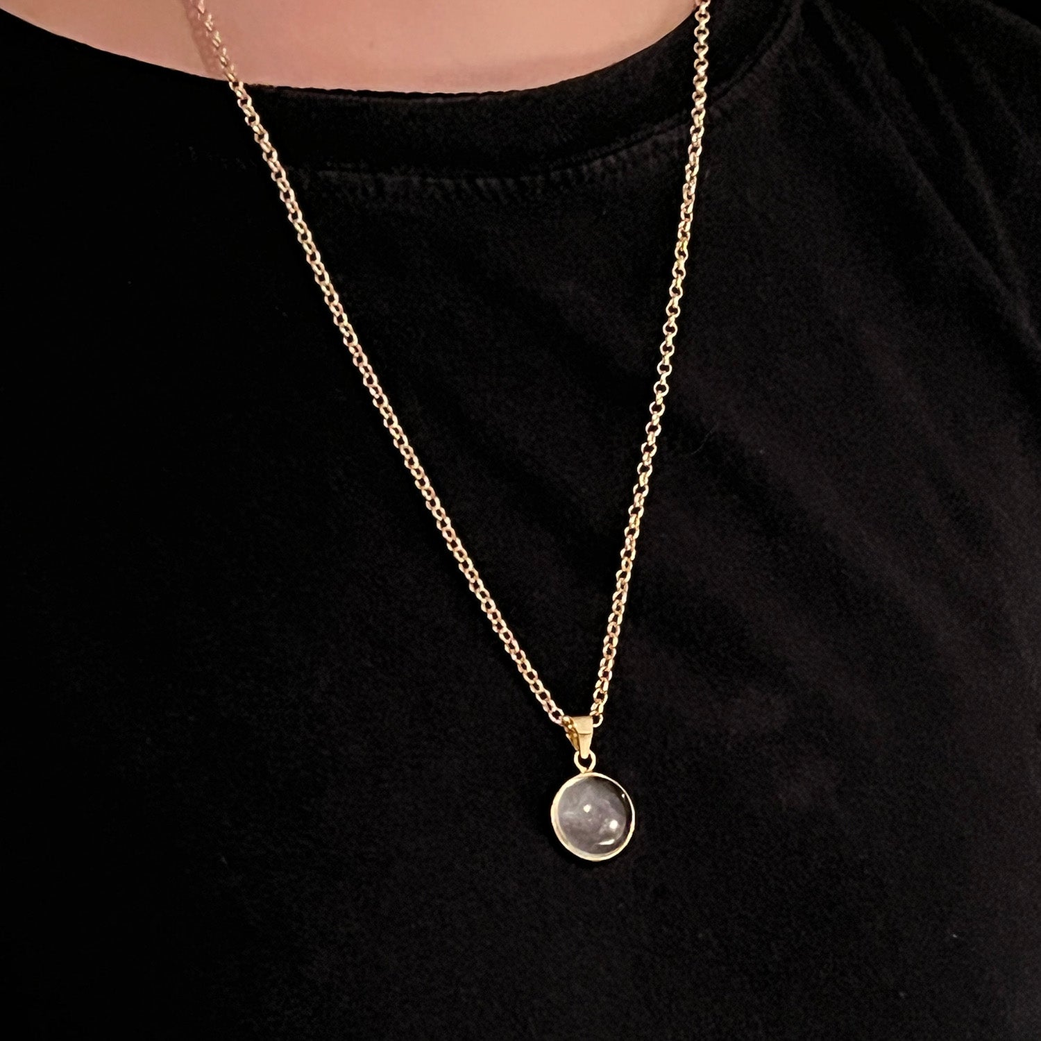 Close up of a gold necklace with a rock crystal pendant on a black jumper