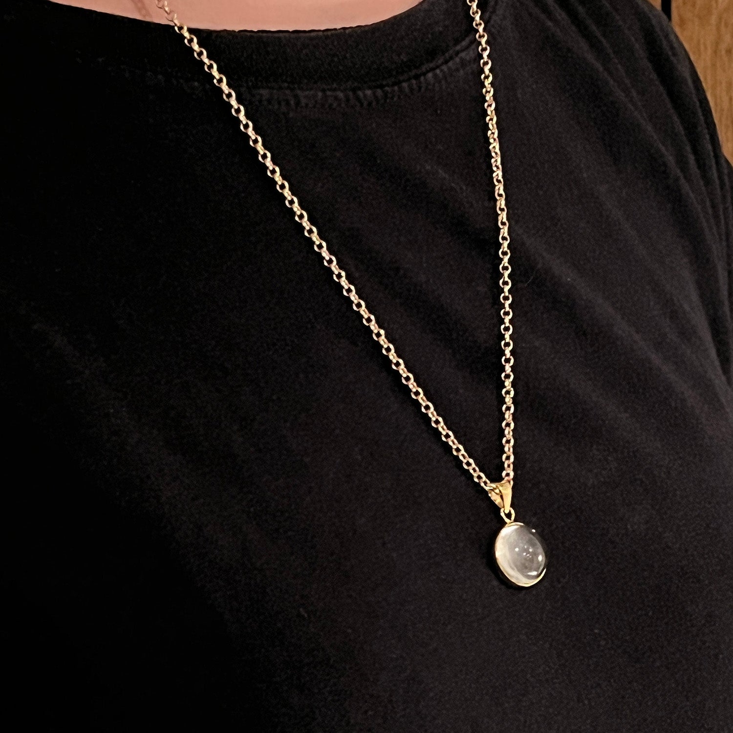 Gold chain necklace with a round pendant on a black shirt