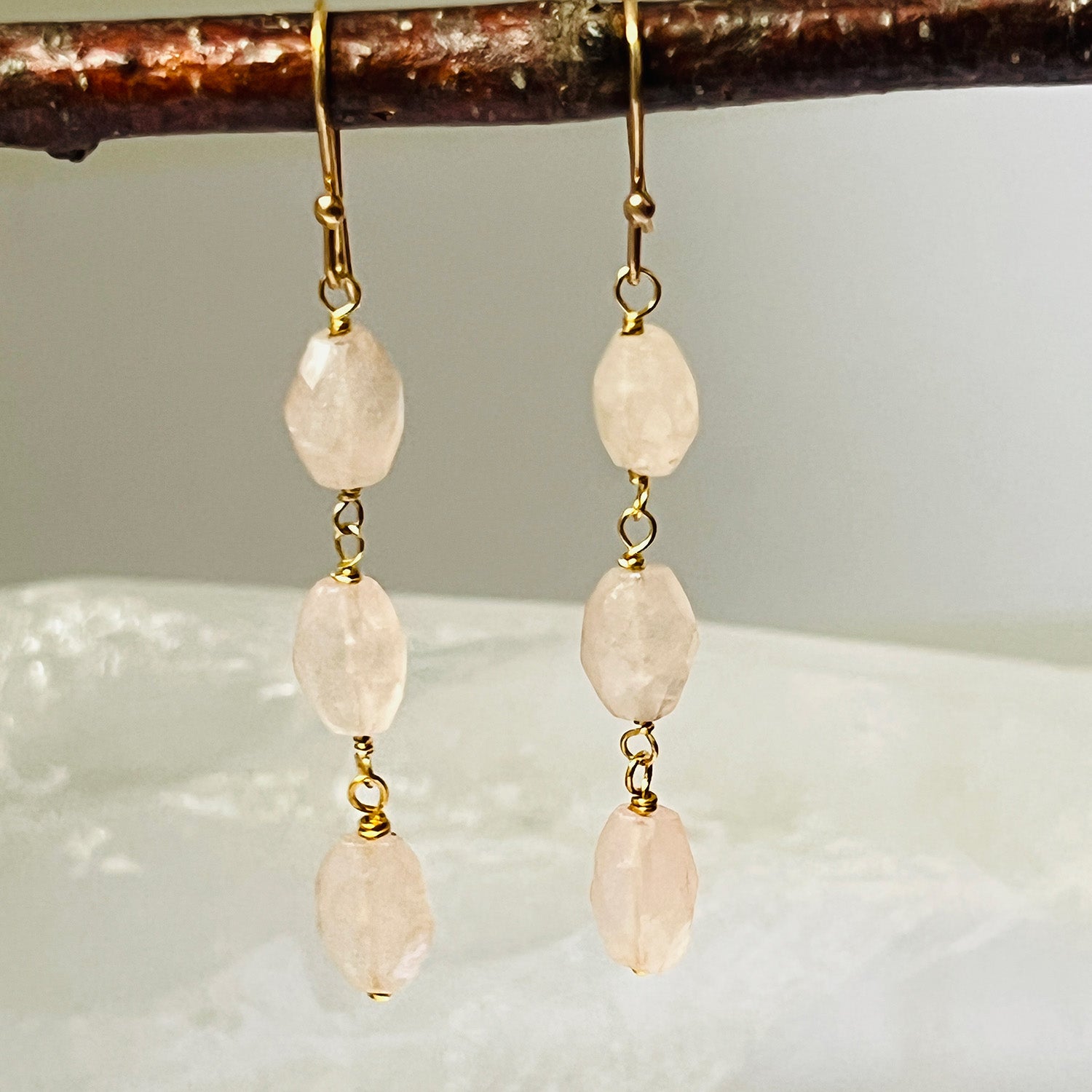Pair of gold earrings with pink rose quartz hanging from a branch.