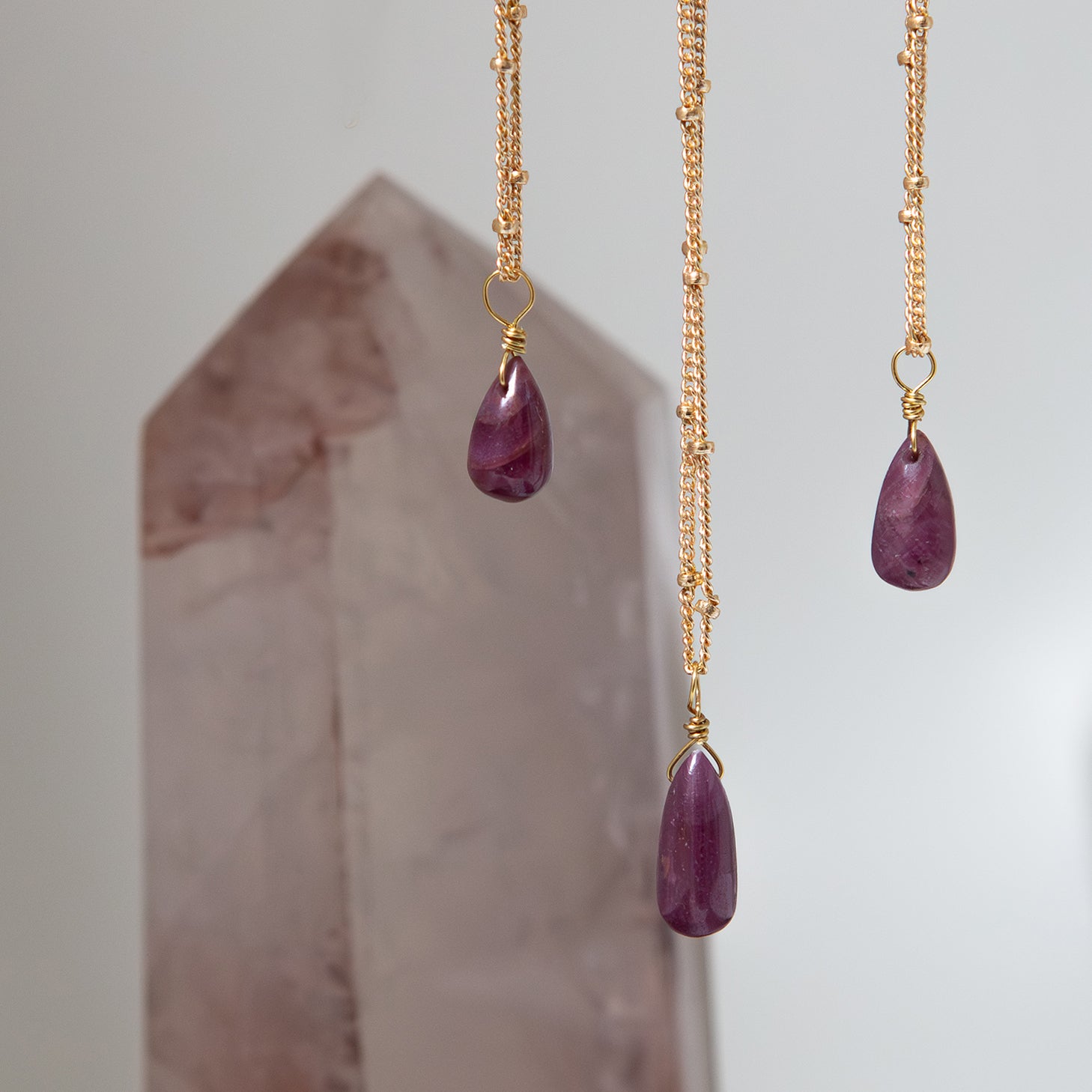 Three gold necklaces with ruby teardrop pendants on a neutral background