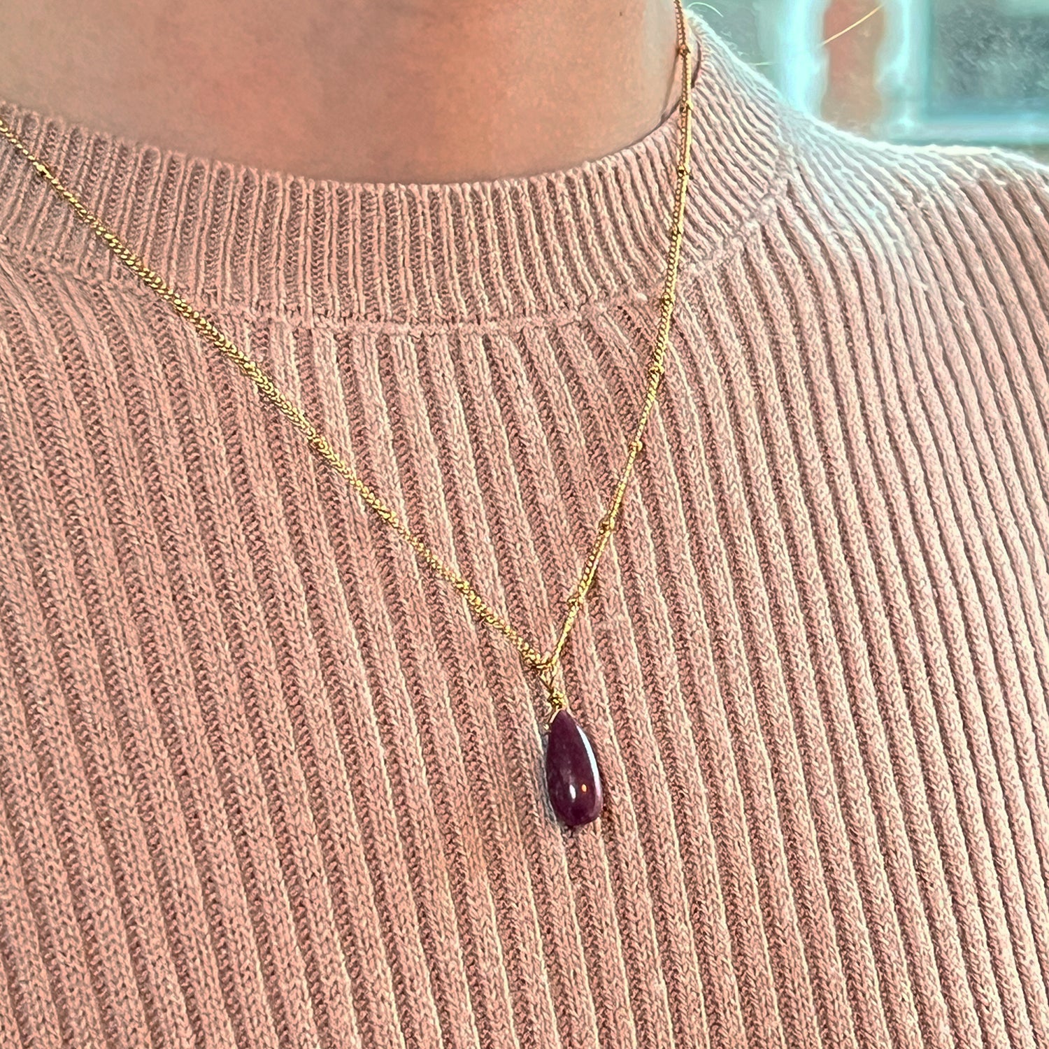 Gold necklace with a ruby pendant on a pink jumper