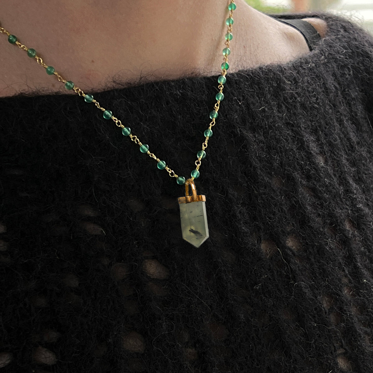 Necklace with green onyx beads and a pendant on a person wearing a dark jumper.
