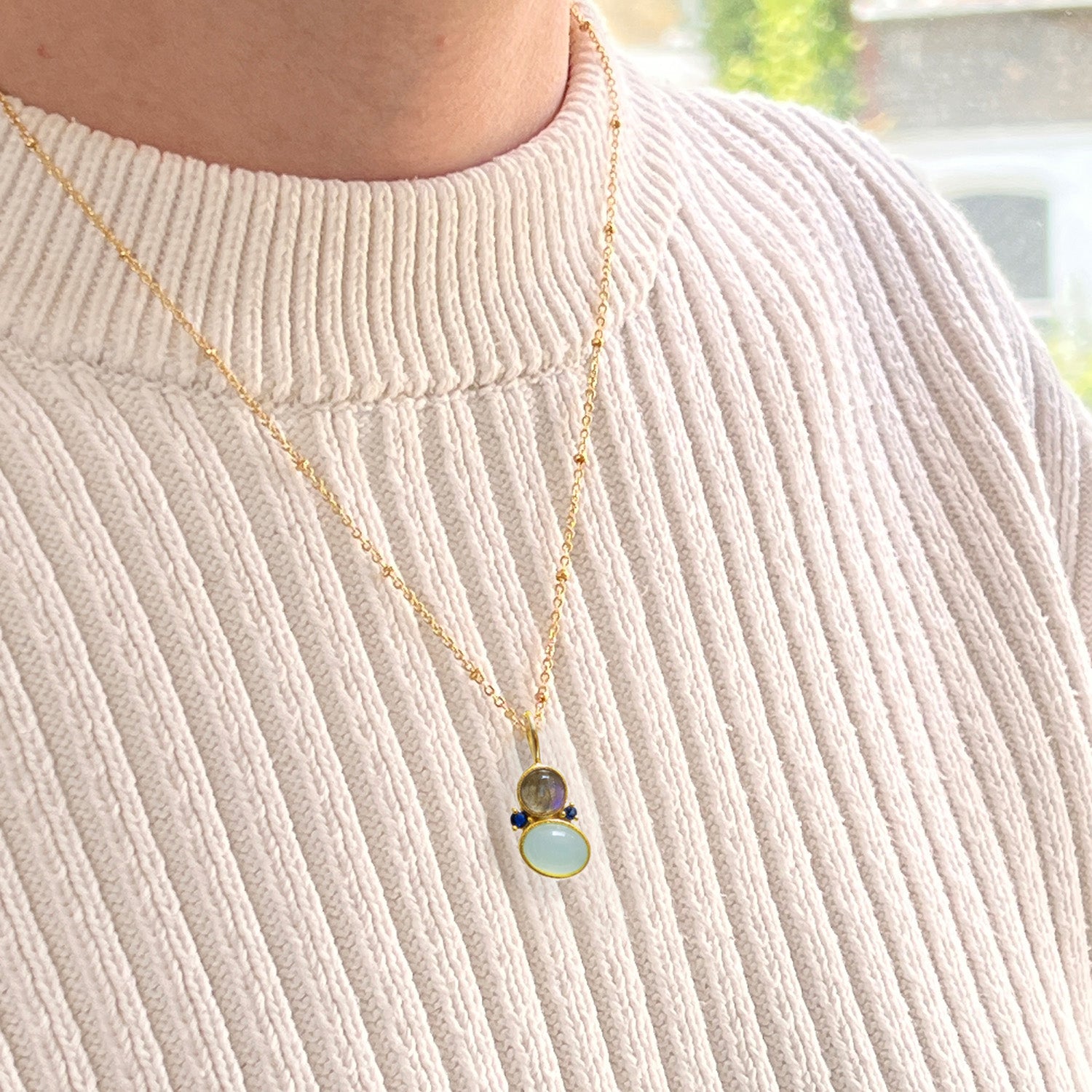 Asymmetric pendant necklace with three stones: Aqua Chalcedony, Labradorite, and Blue Zircon on a person wearing a textured sweater.