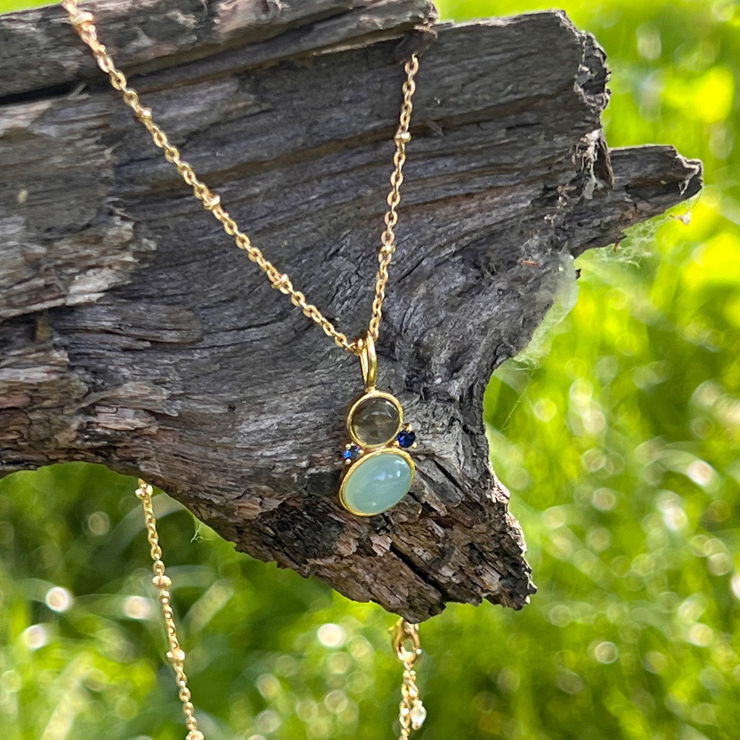 Gold necklace with aqua chalcedony, labradorite and blue zircon pendant on a piece of wood outdoors