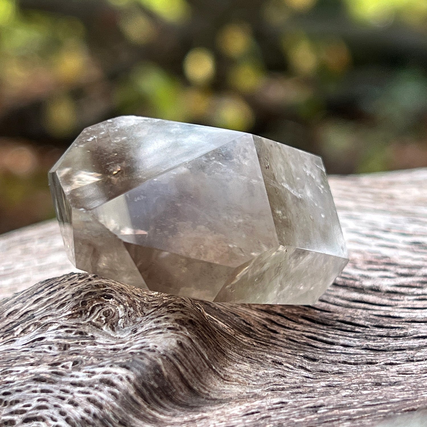 Clear citrine phantom quartz crystal on a textured surface with a blurred natural background