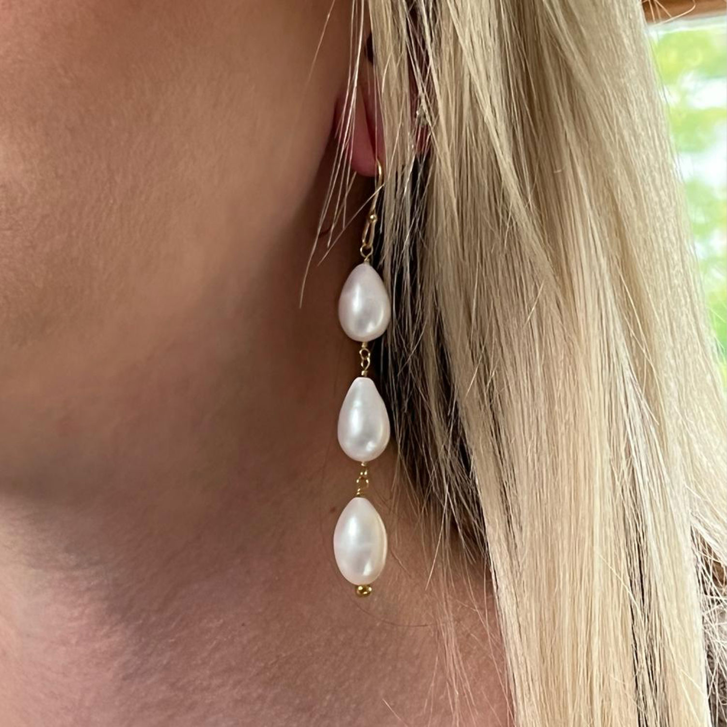 A closeup of a model's ear with a three drop-shaped freshwater pearls earring .