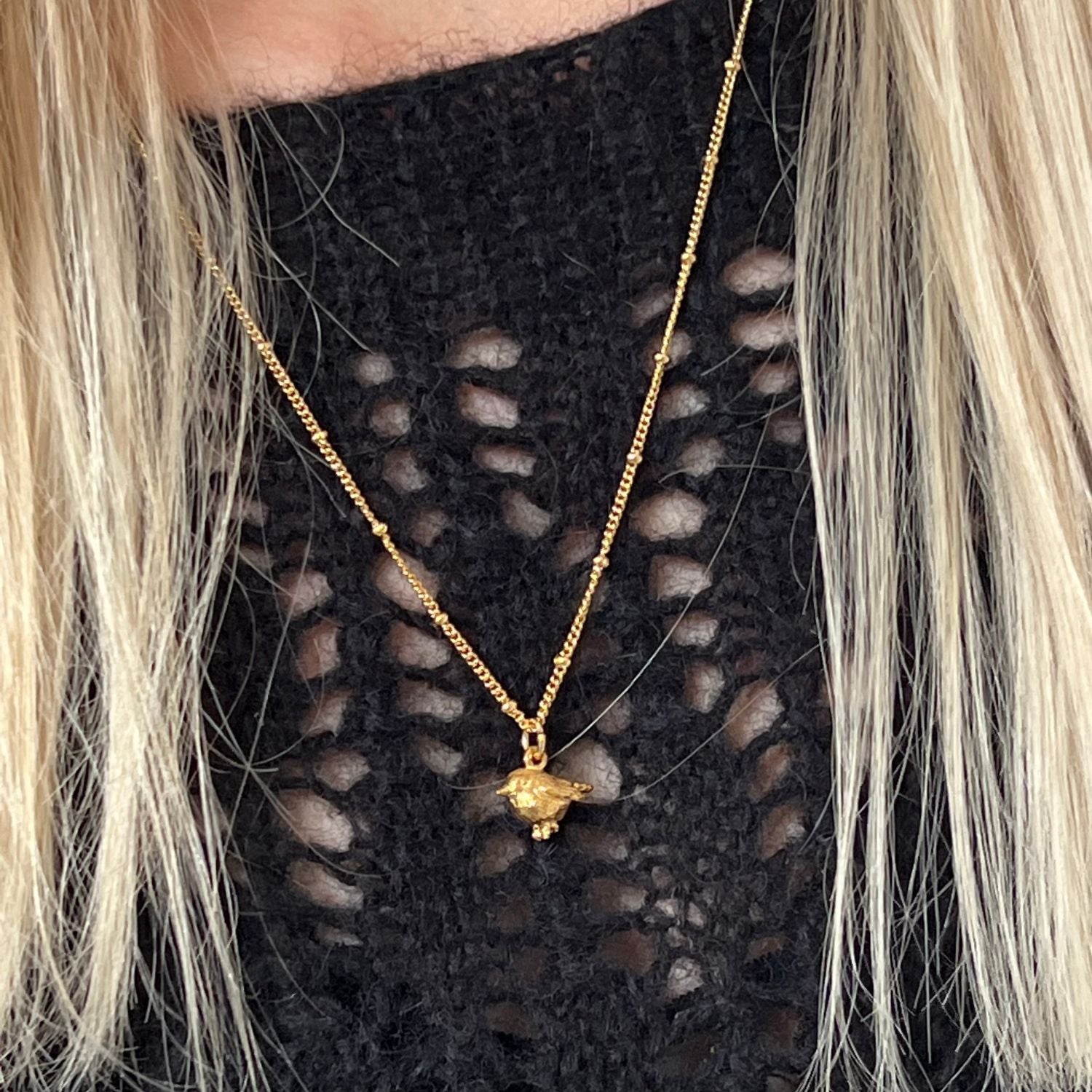 Elegant 22ct gold-plated necklace with a gold Biba chain and cute robin charm. Worn on a black sweater