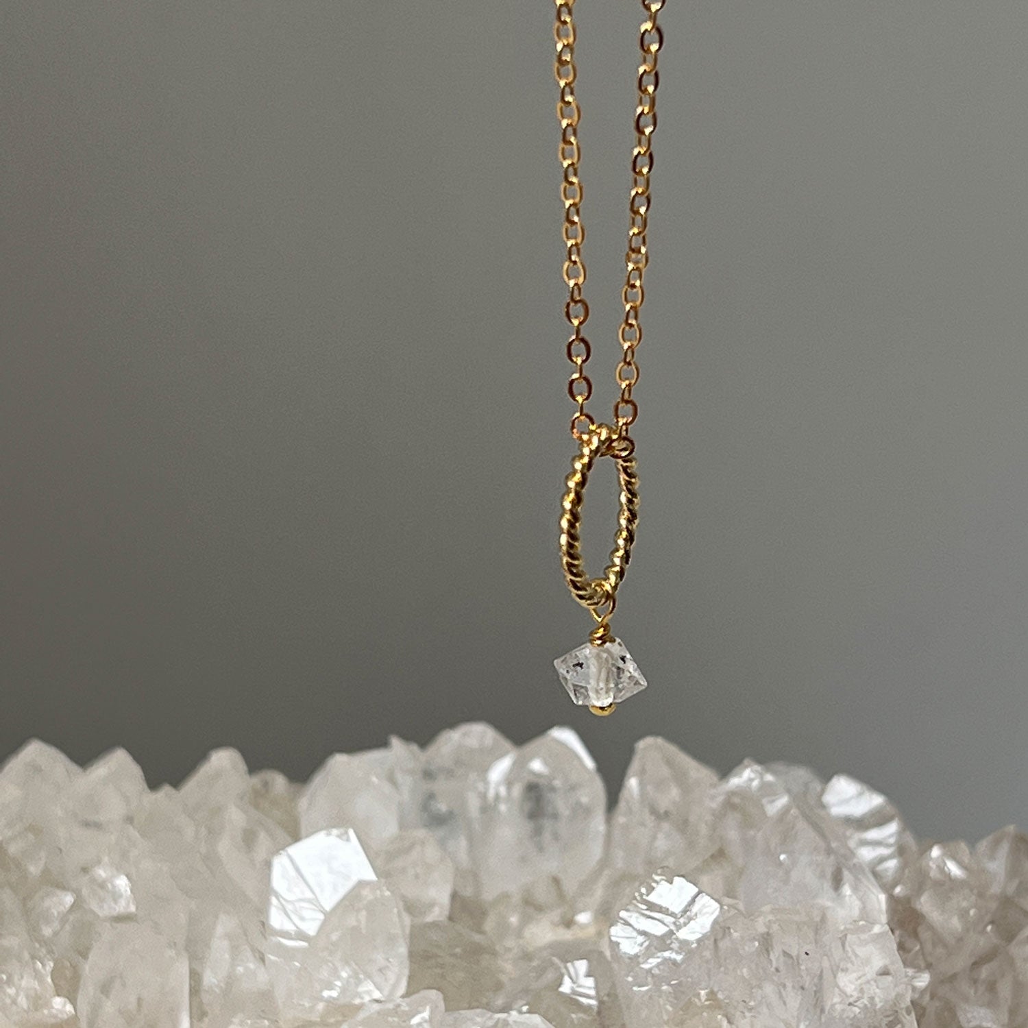 Herkimer quartz diamond pendant on a gold-plated chain with a bed of crystals in the background