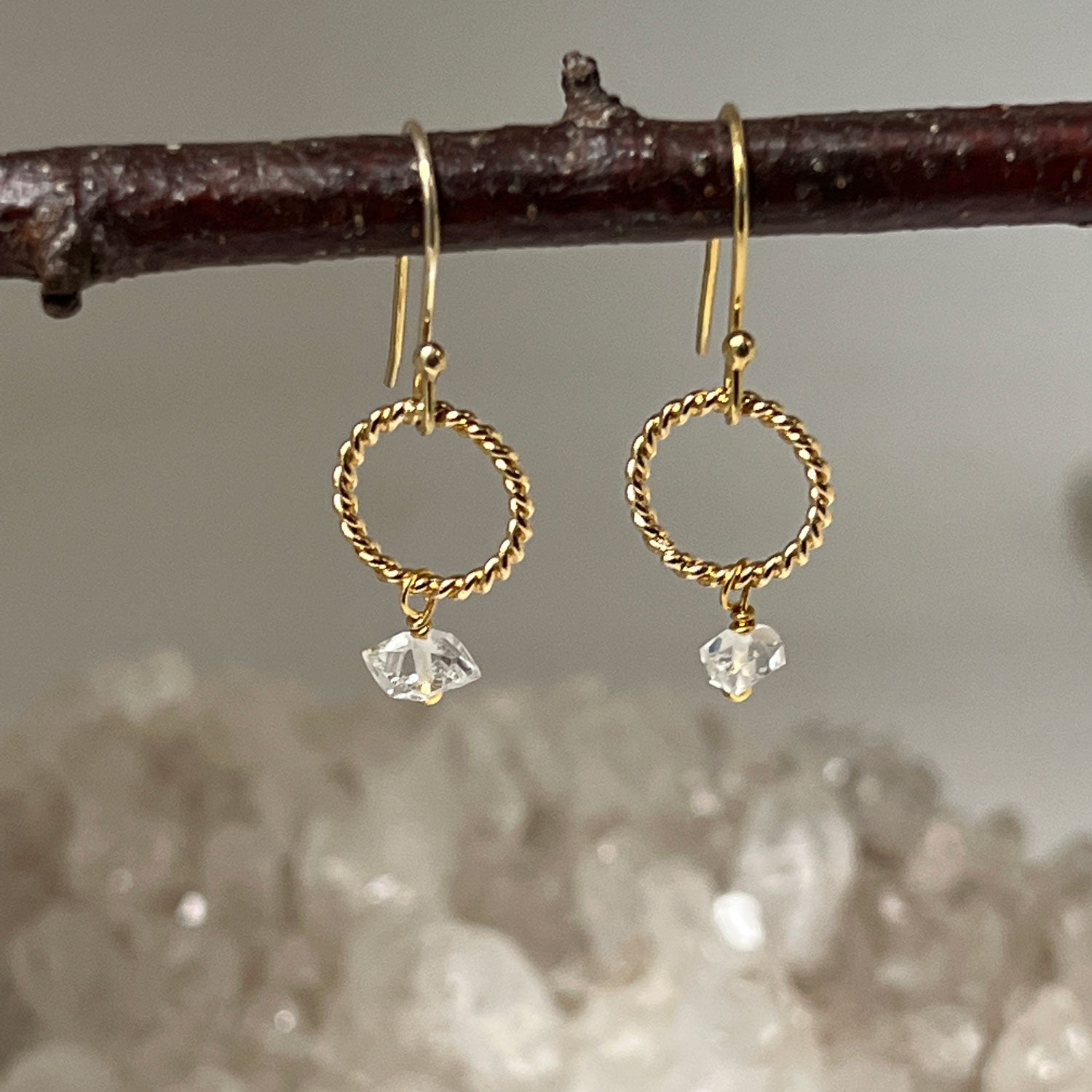 Herkimer quartz diamond earring in a gold-plated loop hanging from a twig