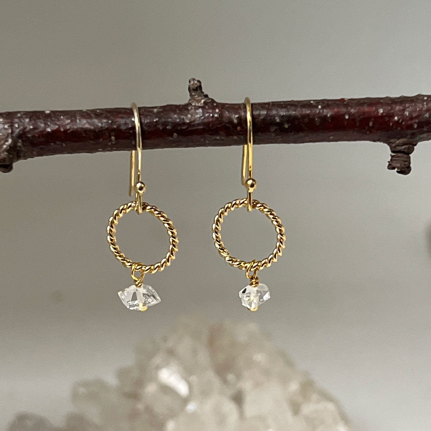 Gold loop earrings with a Herkimer quartz diamond hanging from a twig