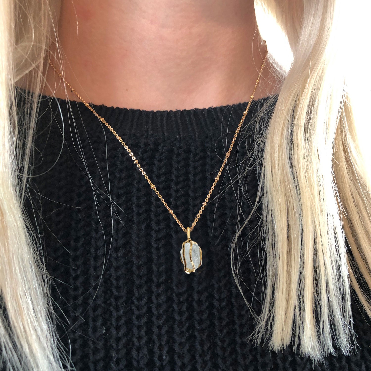 An aquamarine gold pendant worn around the neck of a person wearing a black jumper