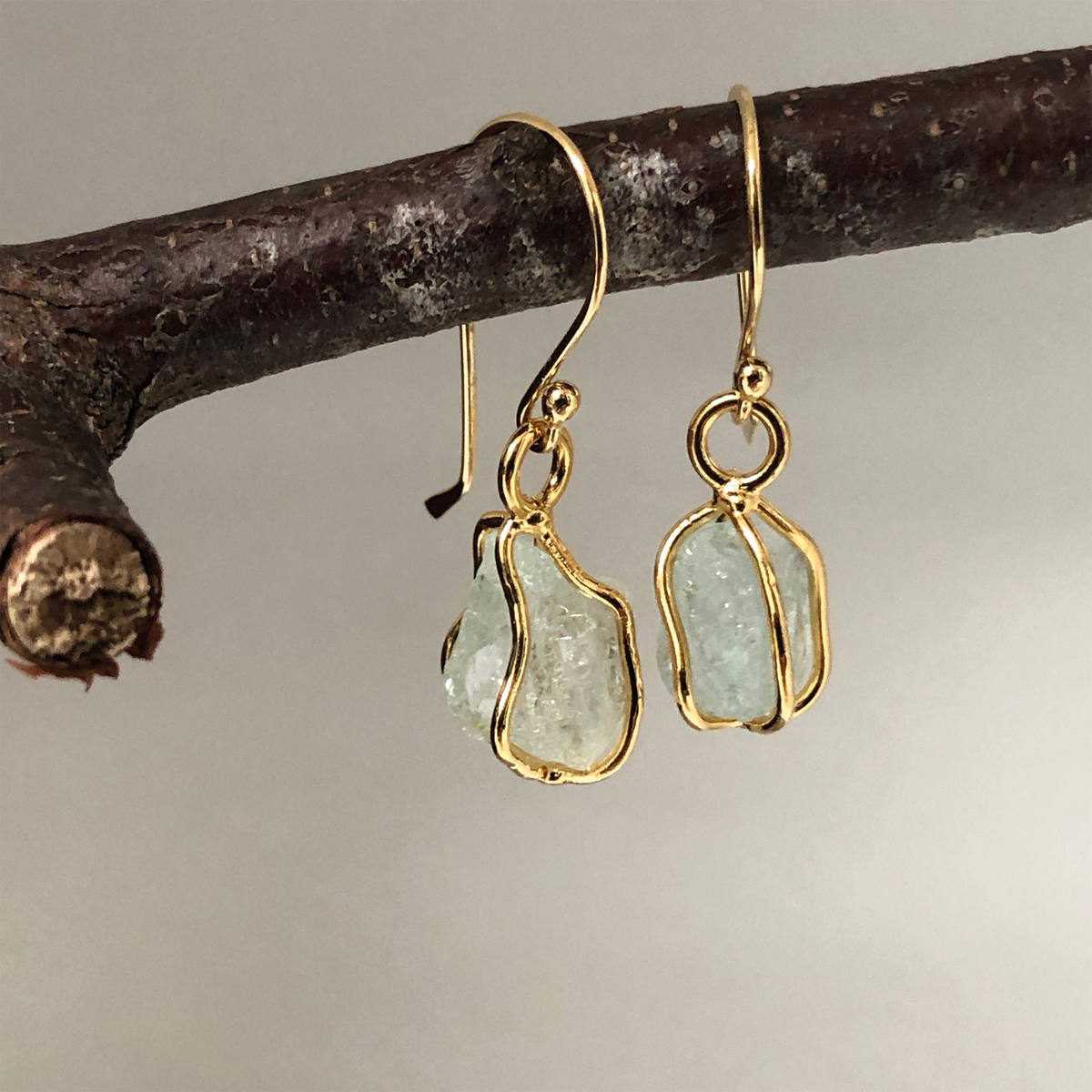 Raw aquamarine earrings handing from a twig