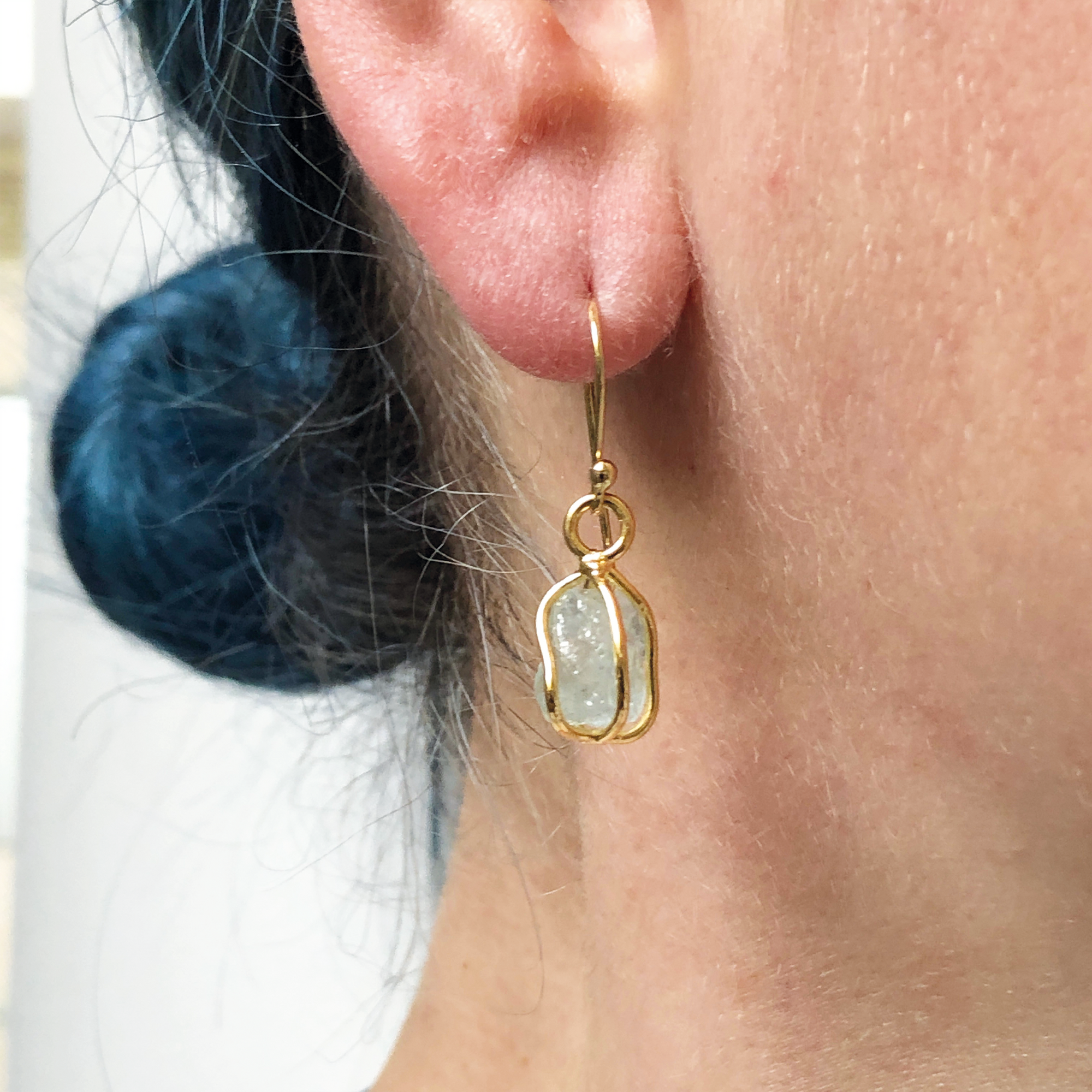 A person wearing a raw aquamarine drop earring