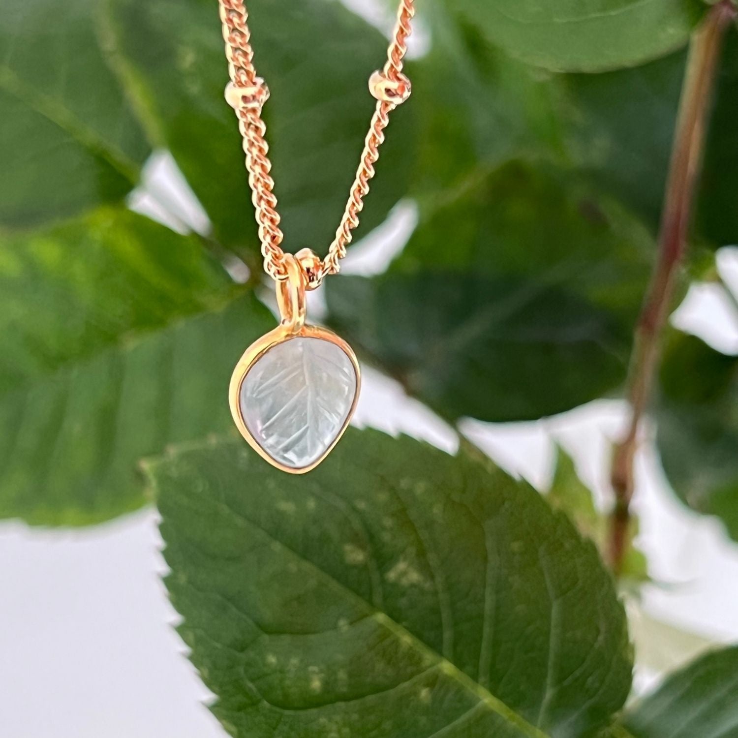 An aquamarine leaf pendant against a backdrop of leaves