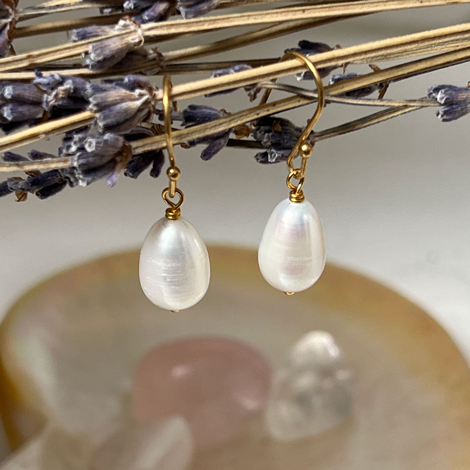 Gold pearl drop earrings hanging from some dried flower stems