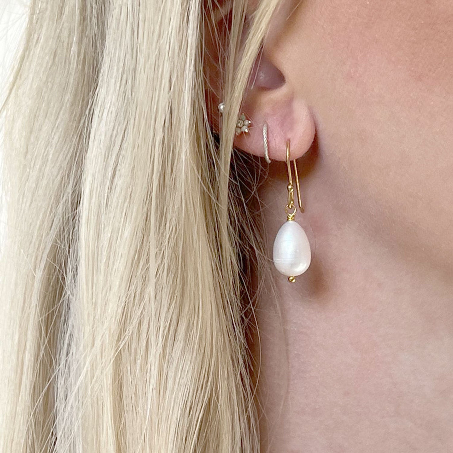 A close-up of a model's ear wearing a pearl drop earring