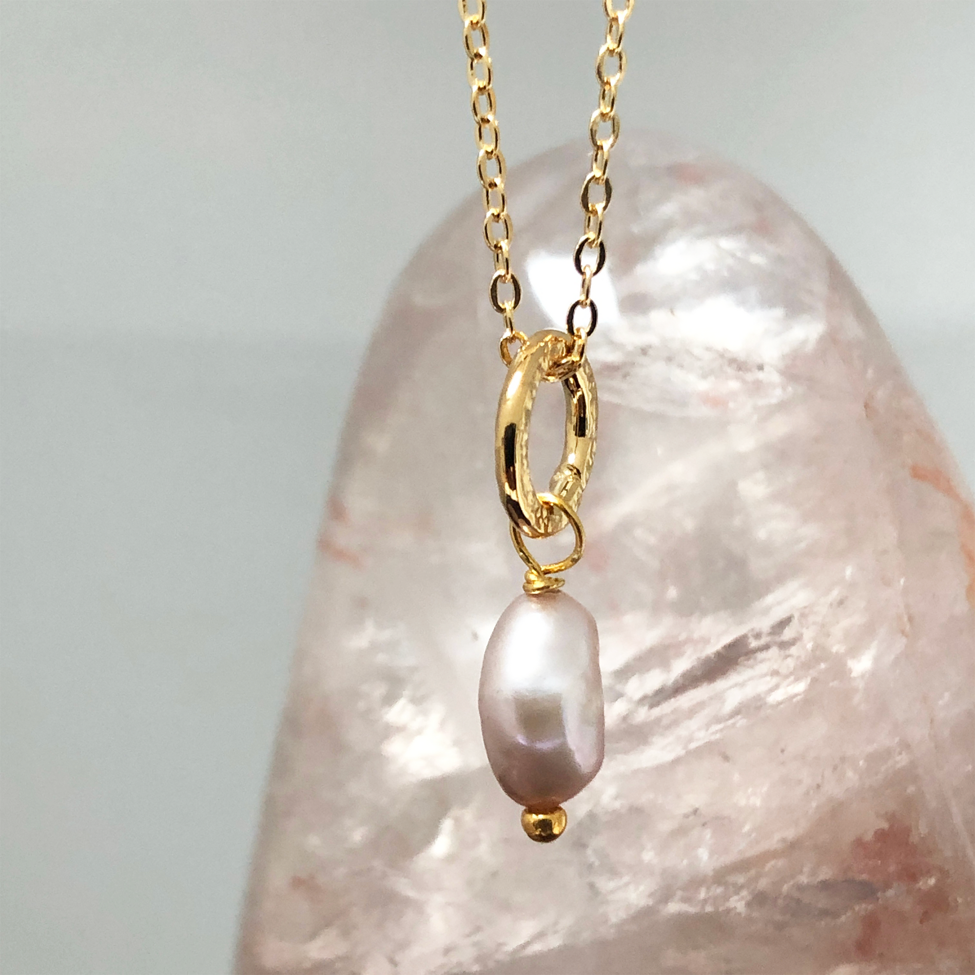 A close-up of a pink pearl gold necklace with a pink crystal in the background
