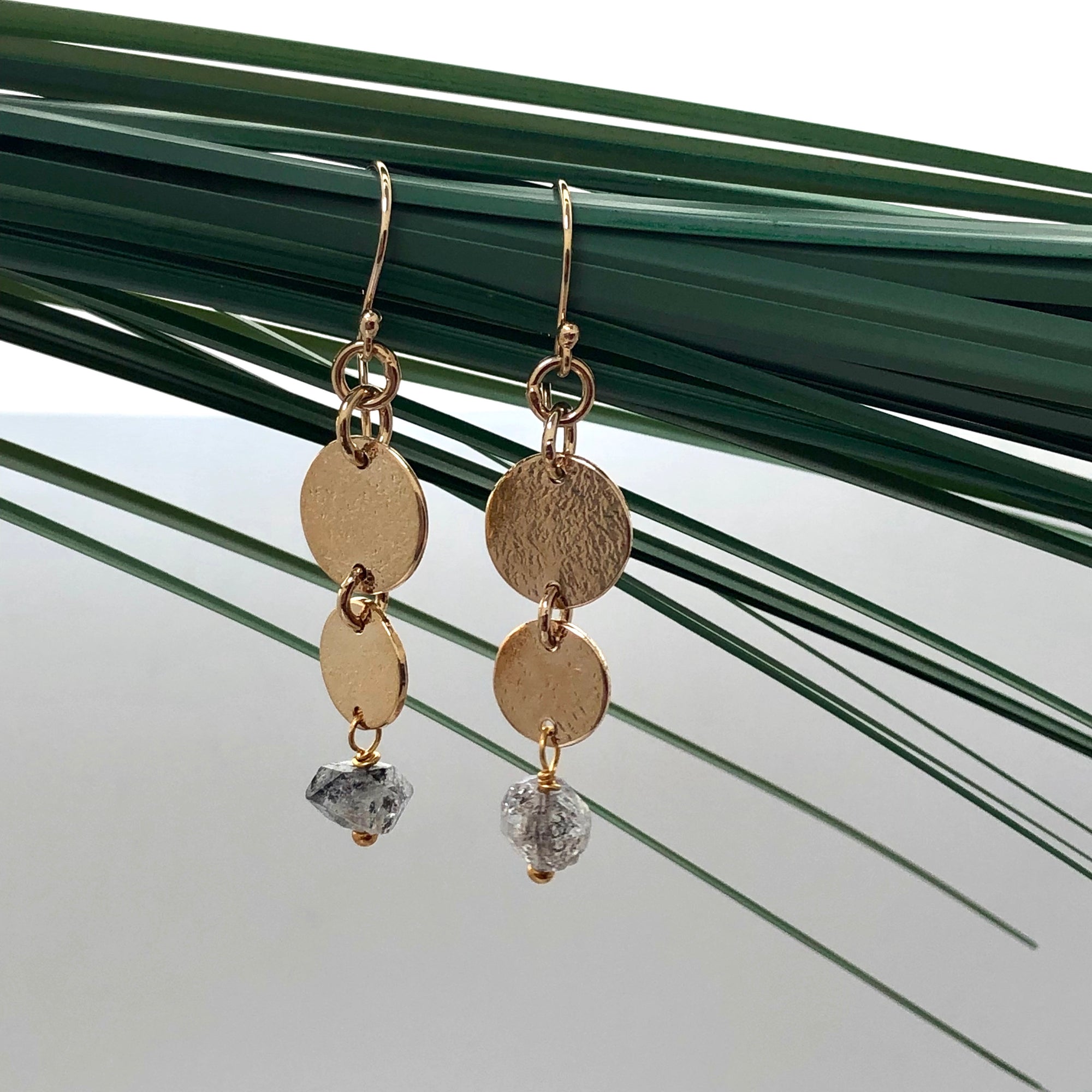 Gold-plated Harmonia Herkimer Diamond drop earrings hangind from some leaves