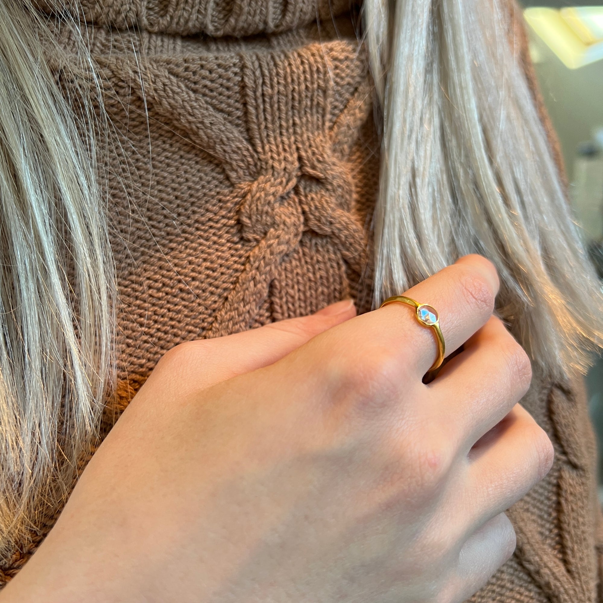 A gold-plated, vermeil-finished ring with a polki cut crystal worn on the hand of someone wearing a brown jumper and blonde hair.