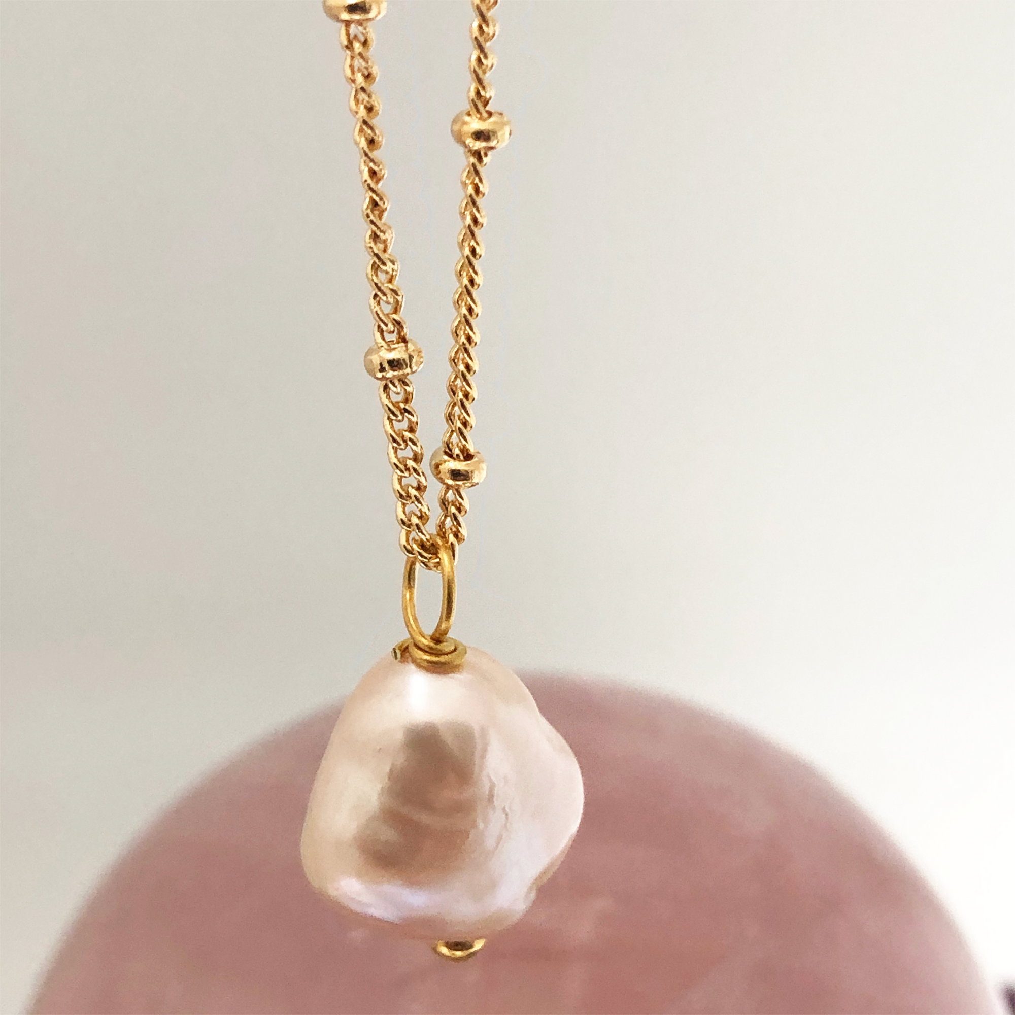 Large Baroque Pink Pearl Pendant on a gold Biba chain with a dark pink crystal in the background