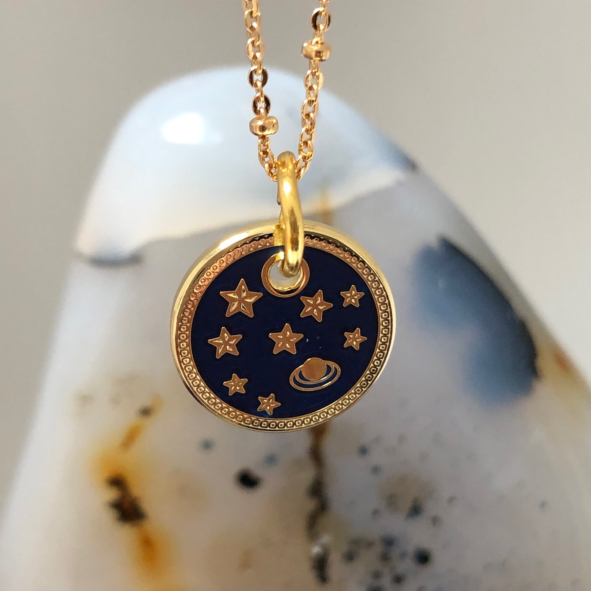 A close up of an enamal medal featuring a planet and stars with a crystal in the background.