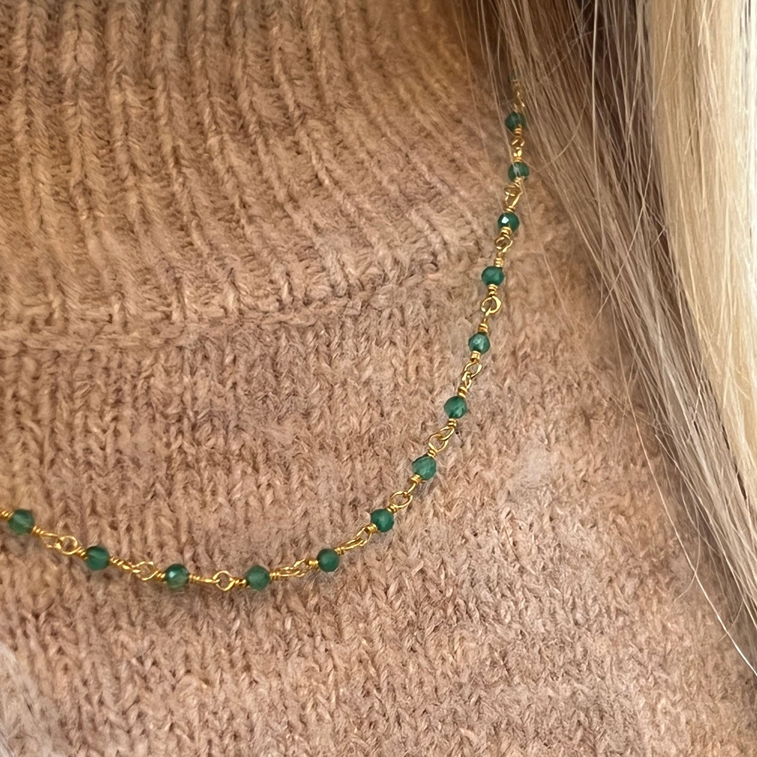 A gold-plated and onyx necklace worn by a model with a brown jumper