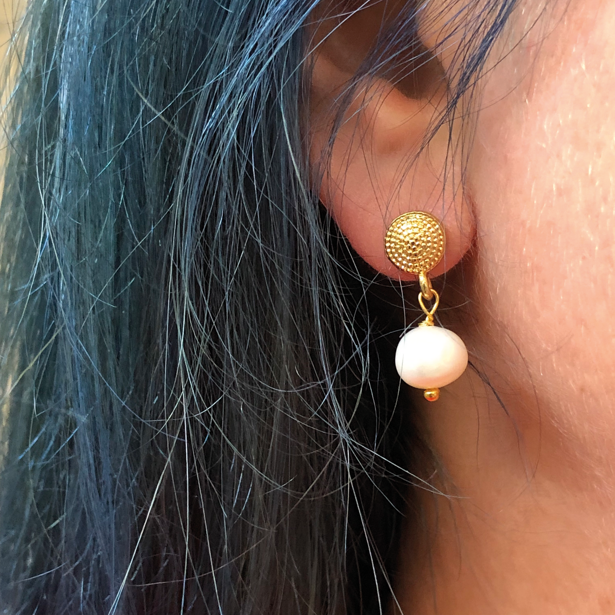 A close up of a model's ear wearing a freshwater pearl gold earring