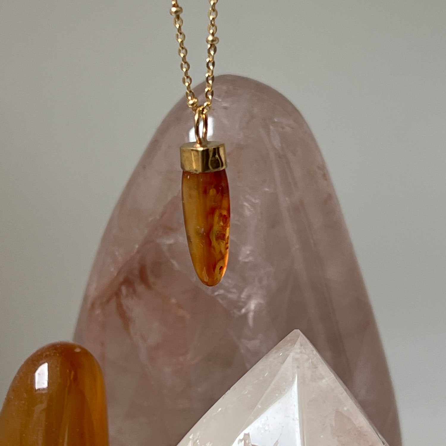 A close up of a gold-plated pendant with a carved orange Carnelian stone, with crystals in the background