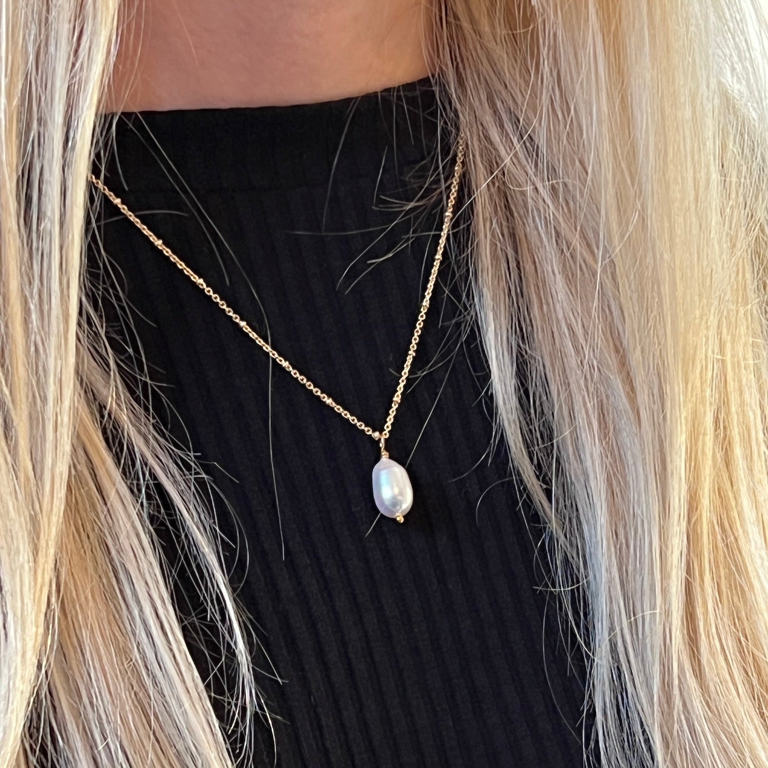 Gold-plated pearl necklace worn by a model with blonde hair and a black sweater